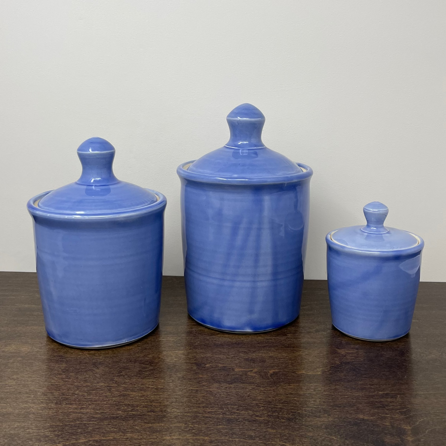 Three blue ceramic jars with lids on a wooden surface against a white wall
