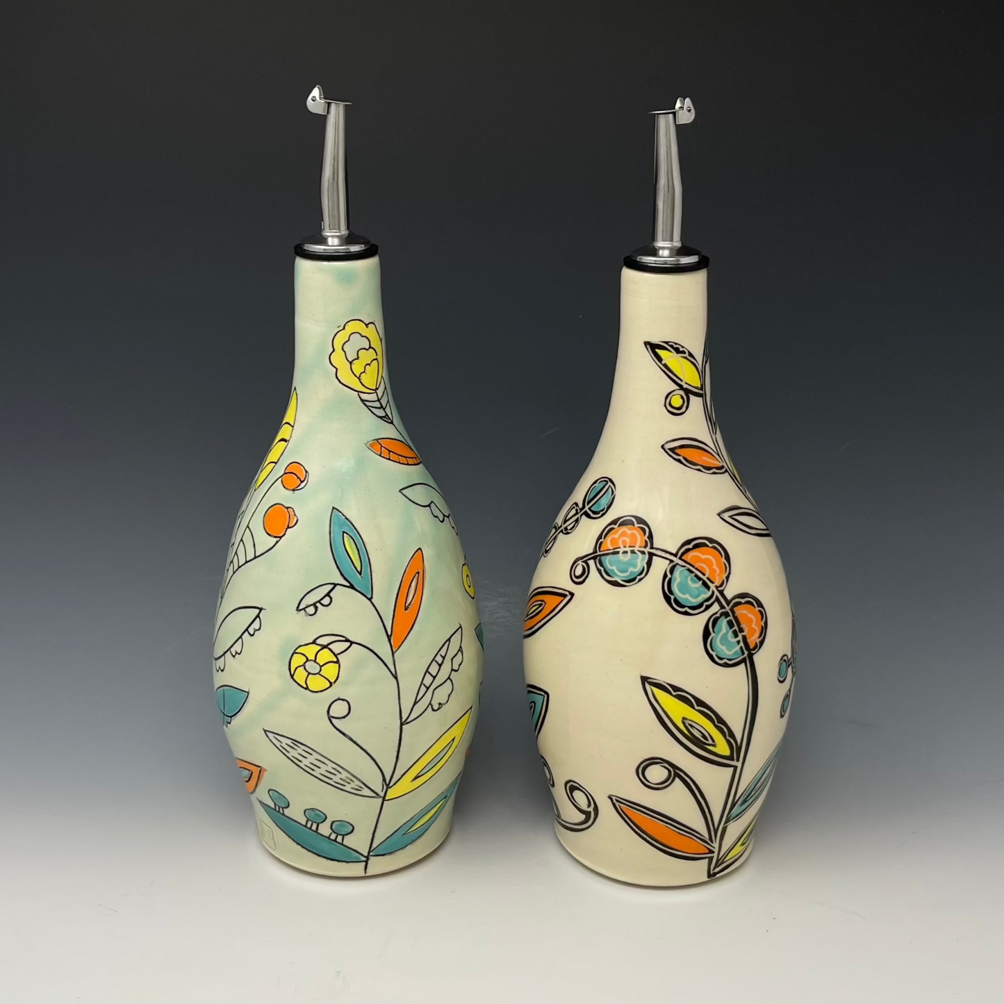 Two ceramic oil bottles with floral designs on a gradient background