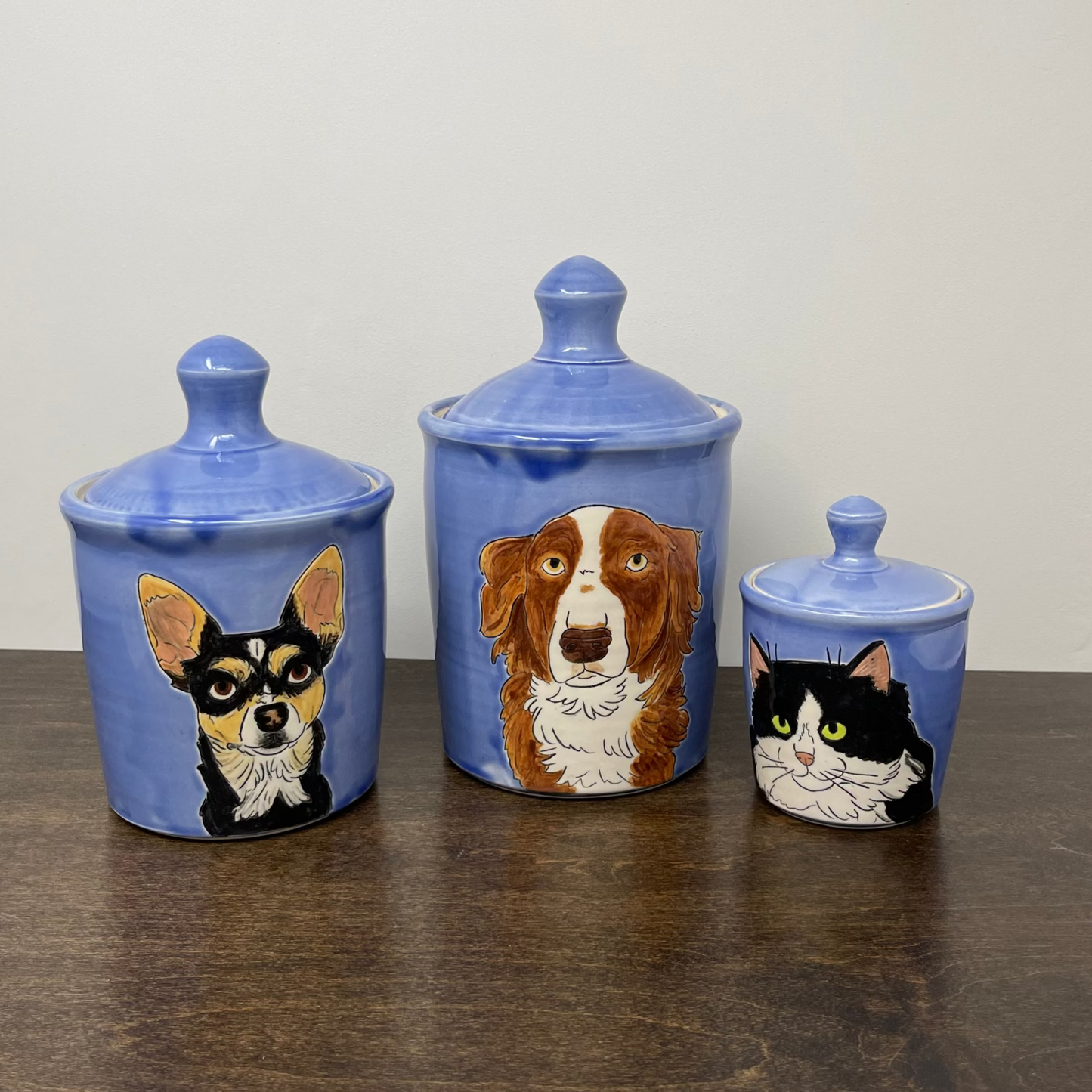 Three blue ceramic jars with pet illustrations on a wooden surface.