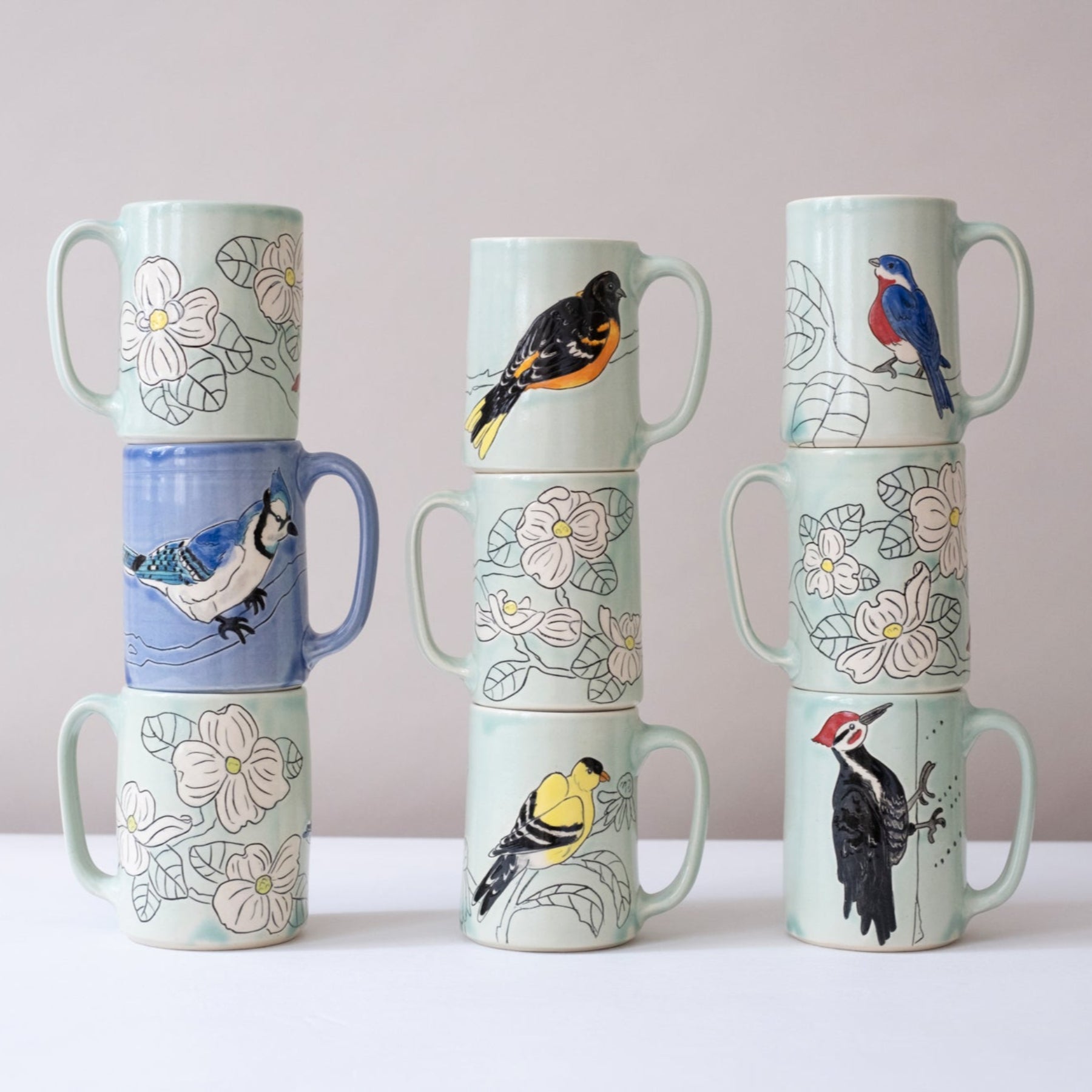 Set of ceramic mugs with bird designs stacked against a plain background
