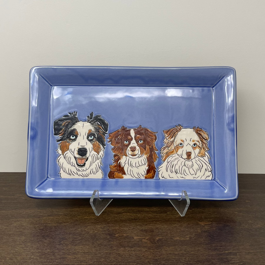 Rectangular blue plate with illustrations of three dogs on a wooden surface.