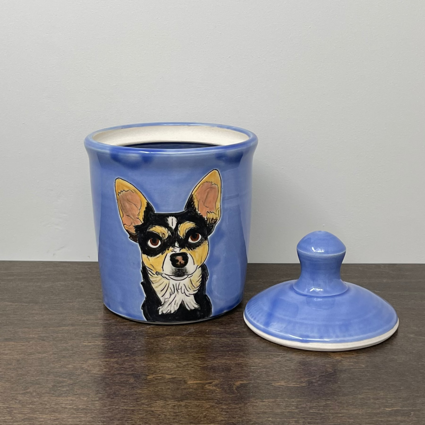 Blue ceramic jar with a lid featuring a dog illustration on a wooden surface.